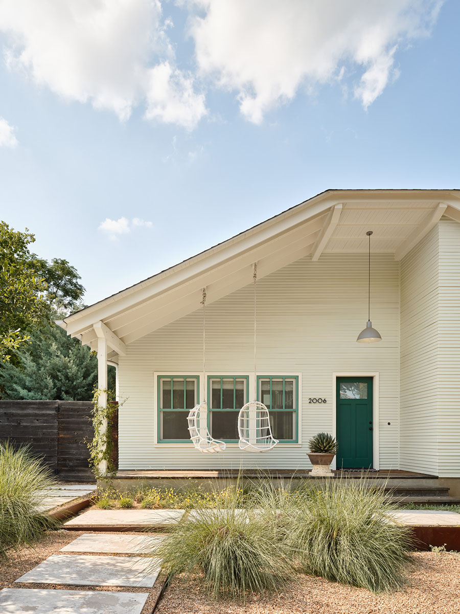 Front porch of modern craftsman home in Austin, TX featuring dual hanging chairs, green-trimmed windows, and xeriscape landscaping – designed by Elizabeth Baird Architecture and built by Texas Construction Company
