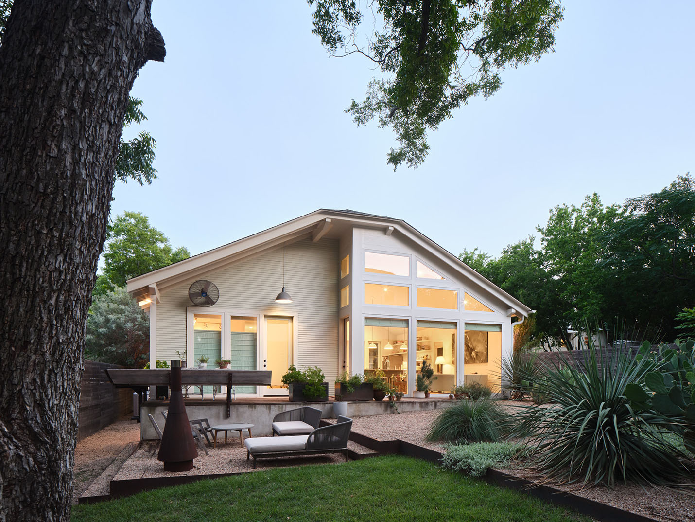Rear view of a custom modern craftsman home in Austin with large windows, outdoor lounge area, native landscaping, and sustainable design by Elizabeth Baird Architecture and Texas Construction Company