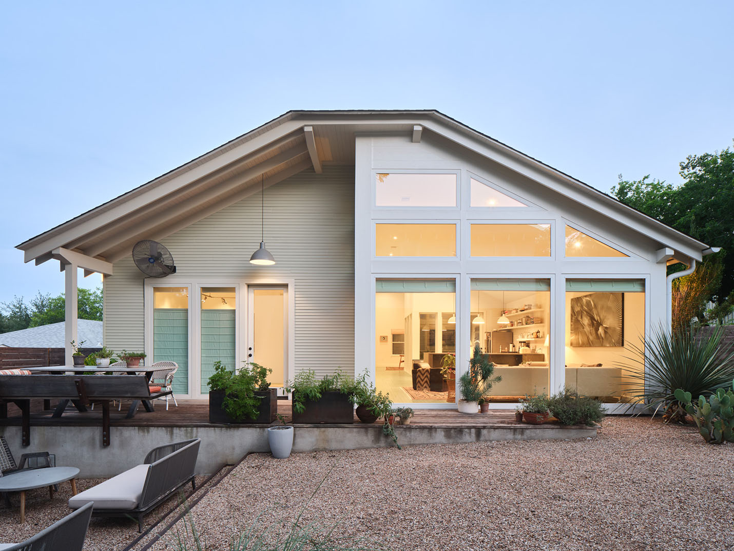 Rear elevation of a modern custom home in Austin, TX with large windows, open interior view, and sustainable xeriscape landscaping by Elizabeth Baird Architecture and Texas Construction Company