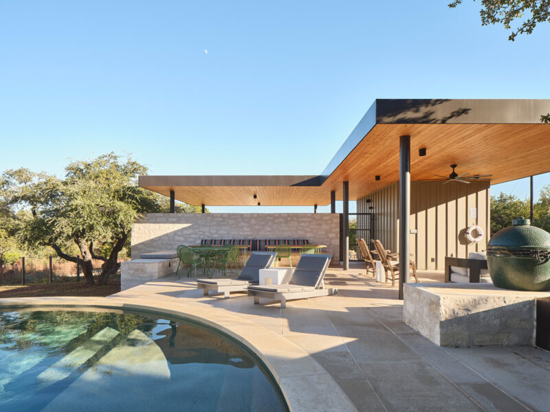 Spacious outdoor pool lounge area at Spicewood custom build house featuring a built-in grill, modern patio furniture, and limestone accents under a wood-paneled roof