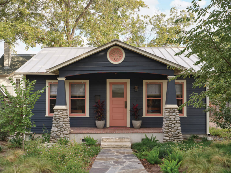 Charming whole house renovation in Austin, TX featuring a navy blue Craftsman-style exterior with coral accents and stone column details