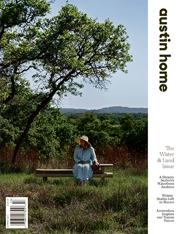 Cover of Austin Home magazine’s Water & Land Issue showing a woman in a light blue dress and sun hat sitting on a bench under a tree with Texas Hill Country in the background, featuring the Reed Park new construction project.