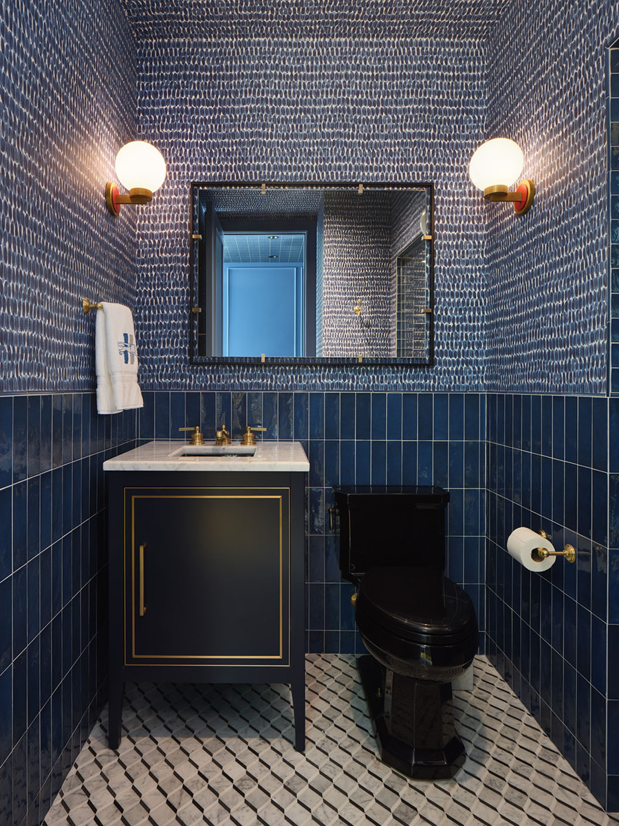 Vibrant powder room with patterned blue wallpaper, dark vanity with gold trim, black toilet, and geometric tile flooring at the 5th Street House Addition in Austin, TX.