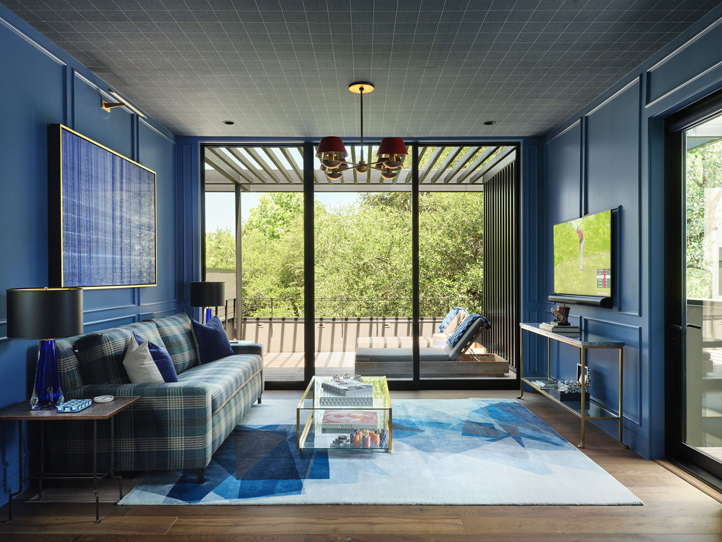 Vibrant blue interior lounge with plaid sofa, modern decor, and glass doors opening to a private patio at the 5th Street House Addition in Austin, TX.