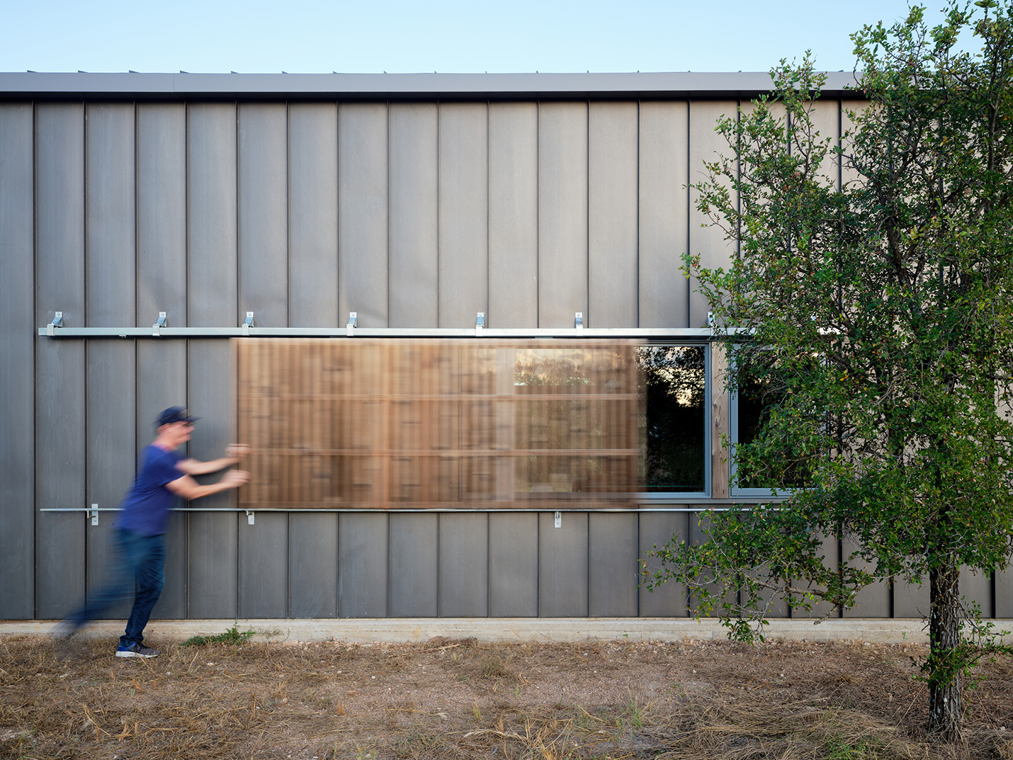 Man sliding custom wood screen over window on modern vertical-paneled home in Austin, TX designed by Ted Young Architecture and built by Texas Construction Company