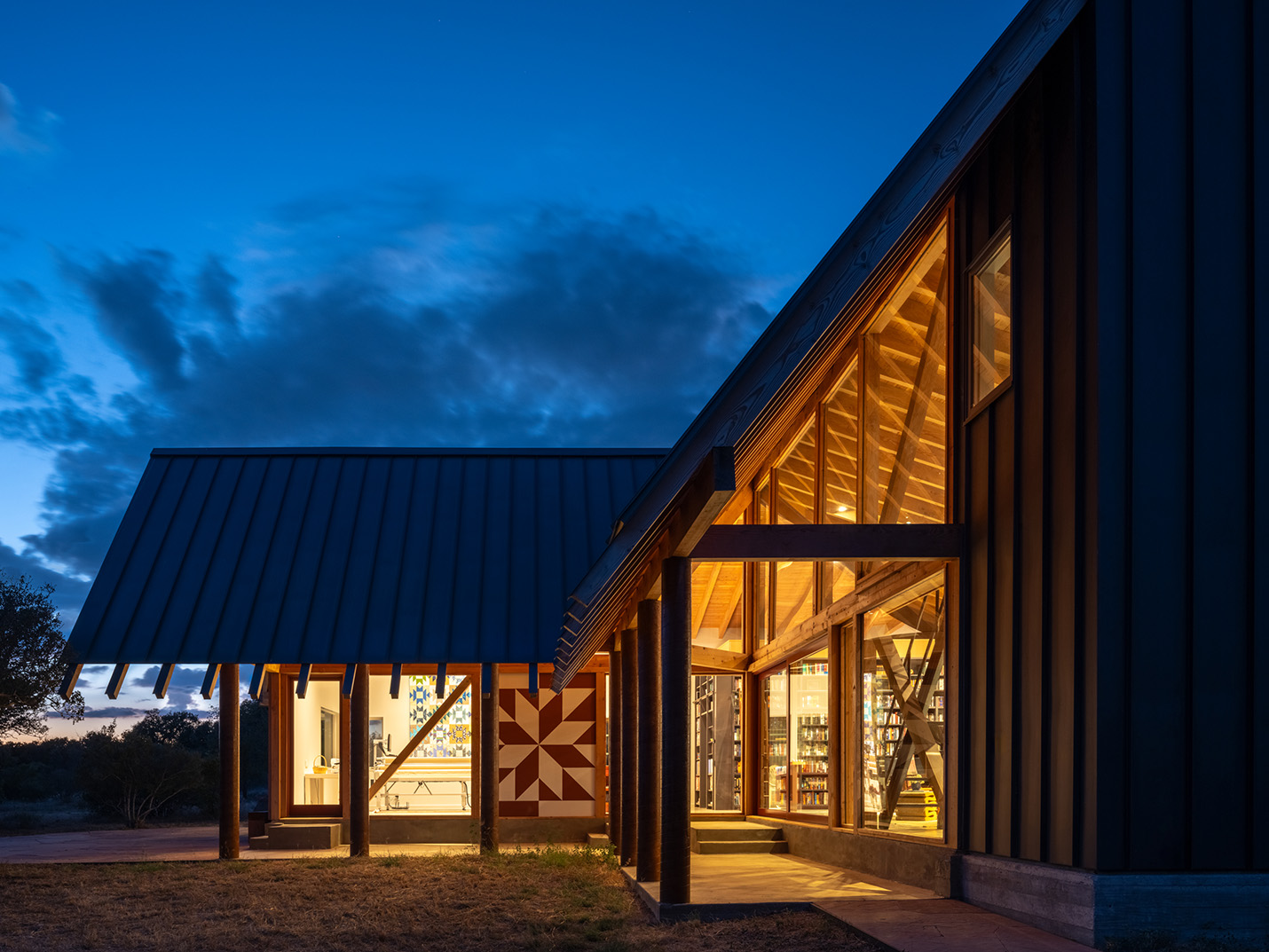 Twilight exterior of modern custom home in Austin, Texas featuring floor-to-ceiling glass, exposed beams, and quilt-inspired paneling, designed by Ted Young Architecture and built by Texas Construction Company