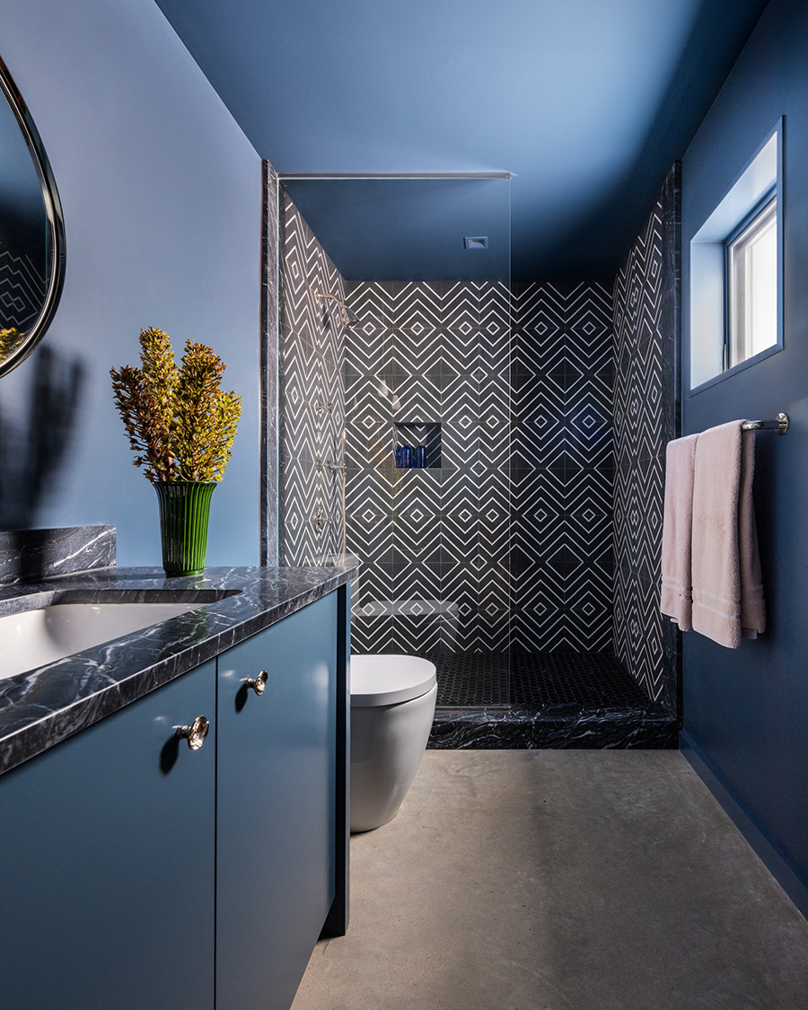 Modern bathroom with geometric black-and-white tile shower, blue vanity, and contemporary finishes in a custom home by Texas Construction Company in Austin, Texas
